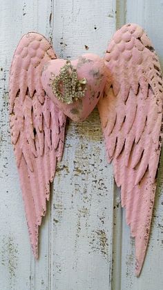 an old pink angel wing hanging on the side of a white wooden door with peeling paint