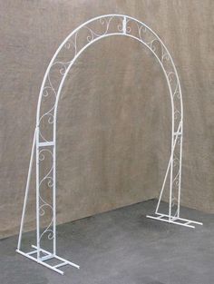 a white metal arch stands in front of a tan wall with an arched top and bottom