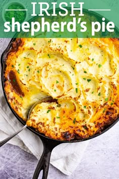 a skillet filled with potatoes and cheese on top of a white cloth next to a spoon