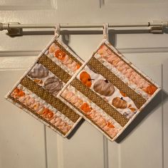 two quilted pot holders hanging from a hook on a white door with pumpkins and acorns