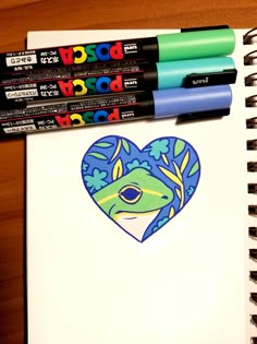 three markers are on top of a notebook with a drawing of a frog in the shape of a heart