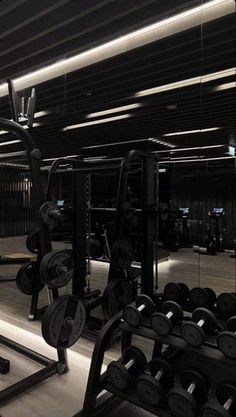 an empty gym with rows of dumbs and weight machines in the foreground, all lit up by recessed lights