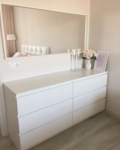 a white dresser sitting next to a mirror in a room with flowers on top of it