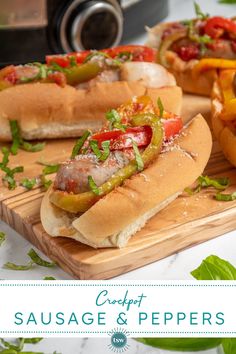 three hot dogs on buns with peppers, onions and tomatoes sitting on a cutting board