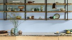 a kitchen with blue walls and wooden shelves filled with plates, bowls and vases