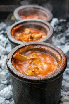 three pots filled with food sitting on top of a pile of fire pit coals