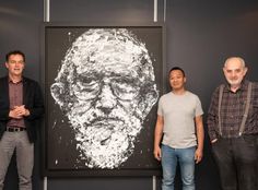 three men standing in front of a painting on the wall with one man looking at the camera