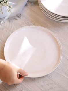 a person holding a white plate on top of a wooden table next to plates and flowers