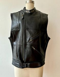 Heavyweight structured black leather vest. Can zip closed in either of the two front zippers depending on desired tightness. The sides are ribbed elasticized leather panels. Lots of seamed detailing and zippered side pockets. Snaps at the collar. With a 1990s DKNY label.  Marked a size large  44" pit to pit  28" length In excellent vintage condition, light overall wear but no flaws to note. Really well made and high quality piece. Moto Vest, Black Leather Vest, Vest Outfits, Leather Vest, Leather Moto, Donna Karan, Womens Vest, Halloween Shopping, Overalls