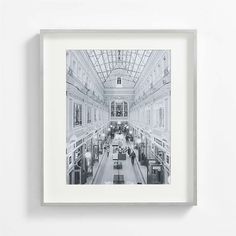 a black and white photo of people walking in a building with glass roofing on the ceiling