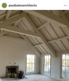 an empty room with two windows and a fire place in the center, surrounded by wood beams