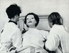 an old photo of two women in white scrubs looking at another woman's face