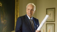 an older man in a suit holding a large piece of paper