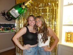 two young women standing next to each other in front of gold foil balloons and streamers