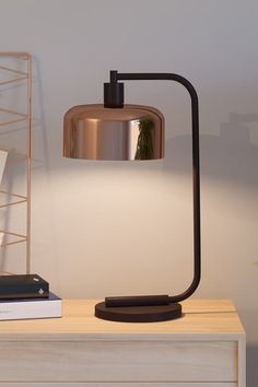 a table lamp sitting on top of a wooden desk next to a book shelf and plant