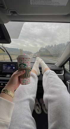 a person holding a cup in their hand while sitting in the driver's seat of a car