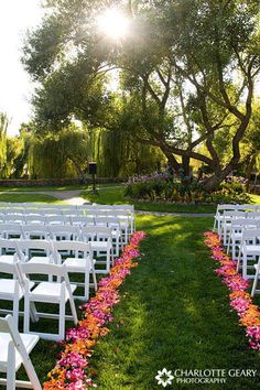 rows of white chairs with pink flowers on them in front of an outdoor ceremony area