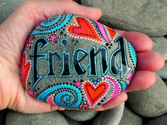 a hand holding a rock with the words friend painted on it, surrounded by rocks