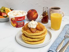 a stack of pancakes sitting on top of a white plate next to fruit and yogurt