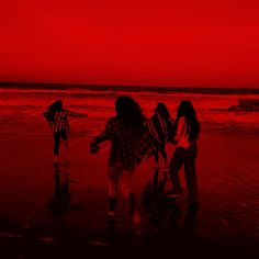 three girls are walking on the beach at sunset with red skies in the background and one girl is holding an umbrella