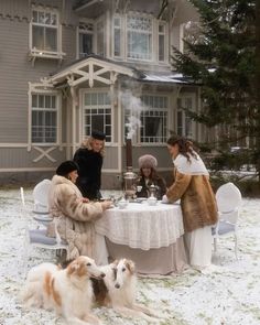 a group of people sitting at a table with two dogs in front of a house