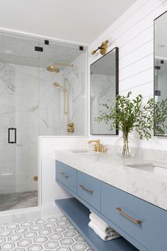 a bathroom with marble counter tops and blue cabinets, gold faucets and mirrors