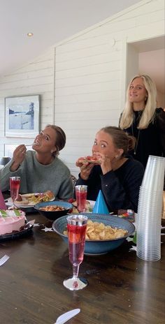 three women sitting at a table with plates of food and drinks in front of them