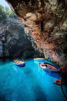 three small boats floating in the blue water next to a large rock formation with trees growing on it