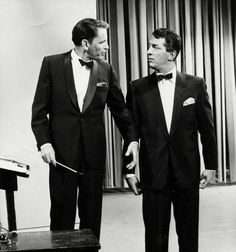 two men in tuxedos standing next to each other near a table with an object on it