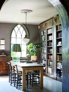 a dining room table with chairs and bookshelves in front of an arched window