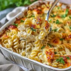 a spoon full of pasta with chicken and parmesan cheese in a casserole dish