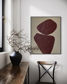 an abstract painting hangs on the wall next to a wooden table with a vase and chair