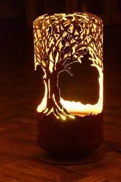 a lit up candle holder with a tree on the front and bottom, sitting on a wooden floor