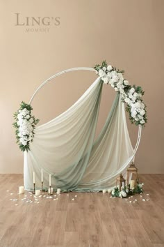 a wedding arch decorated with white flowers and greenery on the floor next to candles