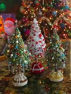 three small christmas trees sitting on top of a table in front of a christmas tree