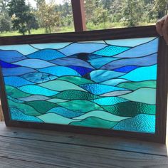 a hand holding up a stained glass window in front of a wooden deck with trees and grass