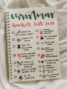 a spiral notebook with christmas stickers on the cover, sitting on top of a bed