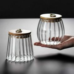 two clear vases sitting on top of a table next to each other, one being held by a person's hand