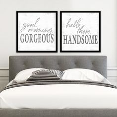 two framed posters on the wall above a bed in a room with white walls and gray headboard