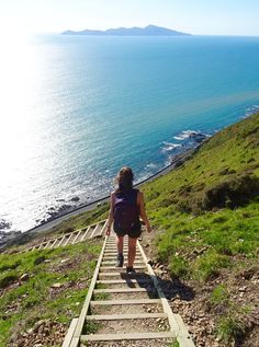 a woman walking up some stairs towards the ocean