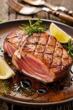 a piece of meat sitting on top of a wooden plate next to lemon wedges