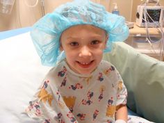 a young child in a hospital bed wearing a blue plastic hat