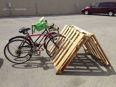 a bicycle parked next to a pile of wooden pallets in a parking lot with a car behind it