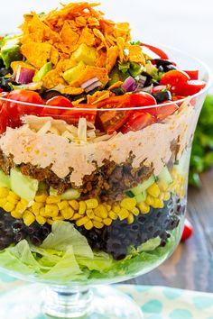 layered taco salad in a glass bowl on top of a table with lettuce and tomatoes