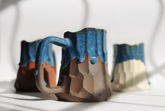 three ceramic mugs sitting next to each other on a white tableclothed surface