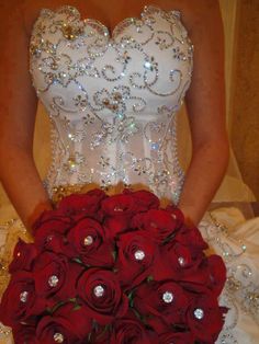 a woman in a wedding dress holding a bouquet of red roses and diamond embellishments