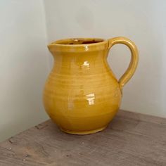 a yellow ceramic pitcher sitting on top of a wooden table next to a white wall