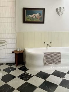 a white bath tub sitting next to a toilet in a bathroom under a painting on the wall