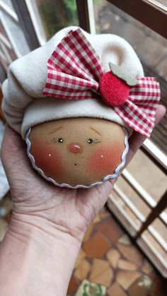 a hand holding up a small doll with a red bow on it's head