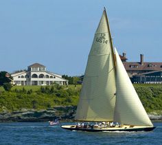 a sailboat sailing on the water near a large house and some houses in the background